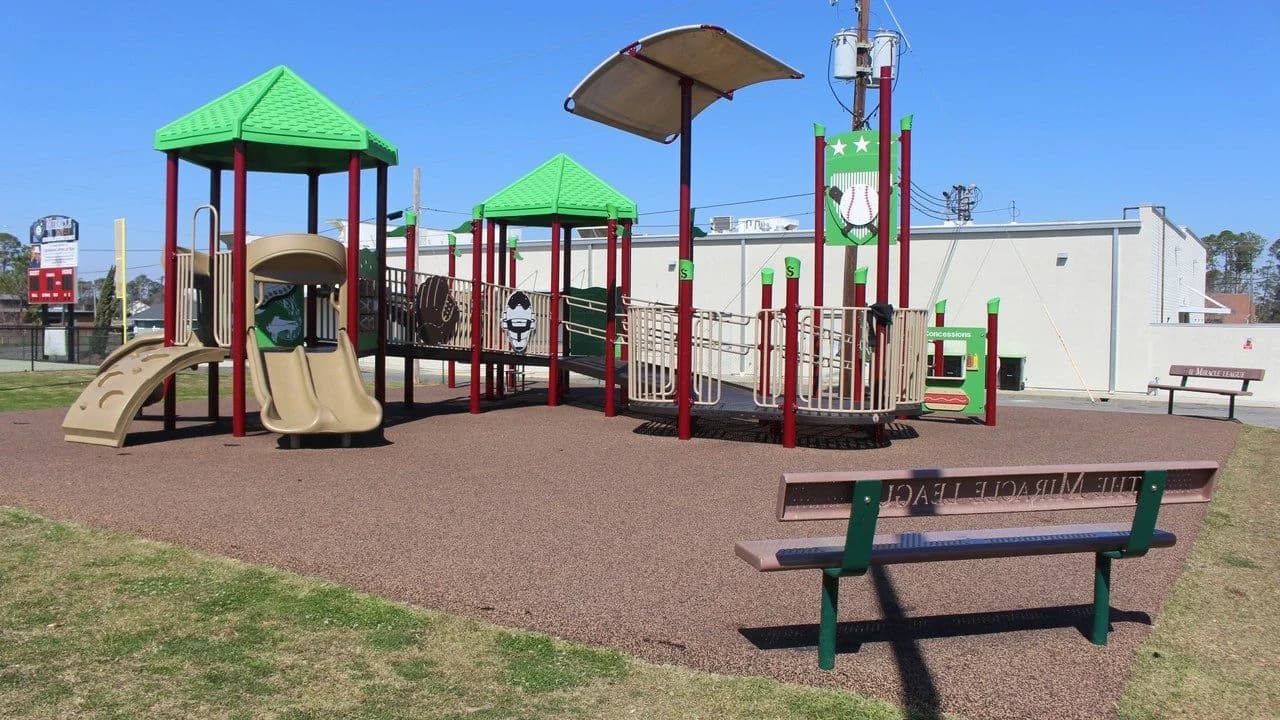 Empty outdoor playground with tan slides and a green climbing structure under a blue sky; no people visible