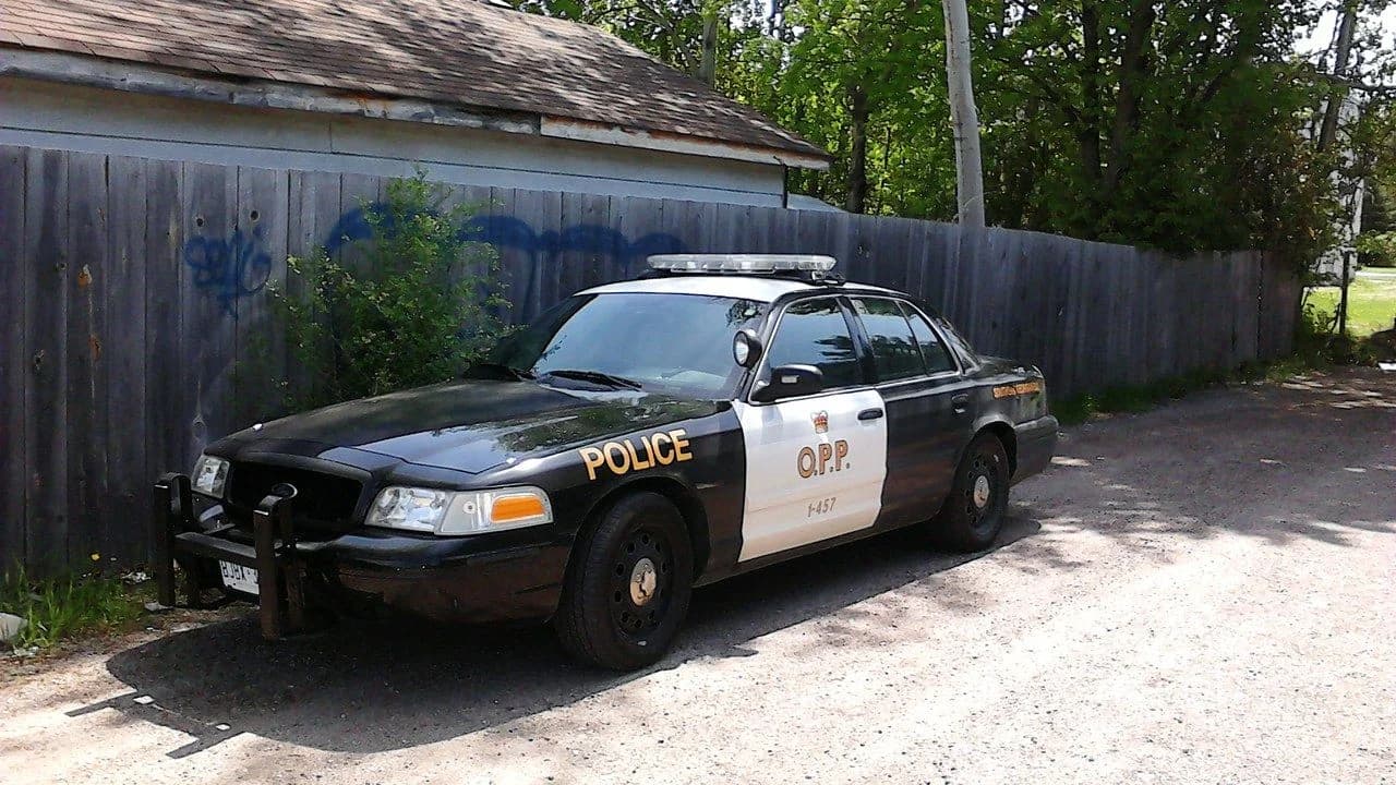 A parked black-and-white Ontario Provincial Police cruiser on a gravel driveway; no people visible.