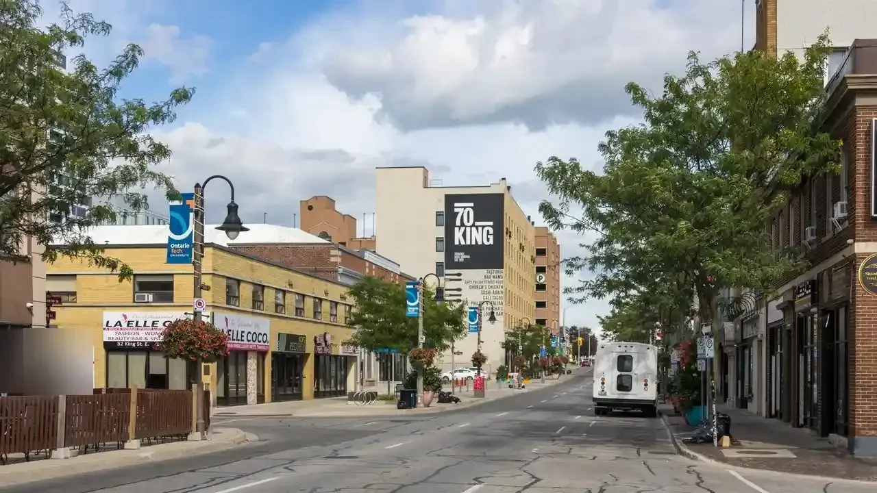 King Street in downtown Oshawa looking east, with shops, restaurants, street banners and trees.